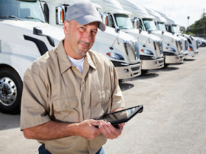 Truck driver in front of big rigs with digital tablet